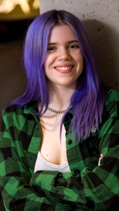 student with long purple hair, arms crossed