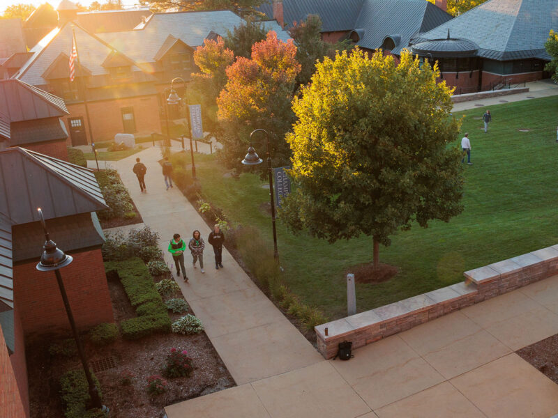 students walk alongside fall trees and campus building as the sun sets overt he lake