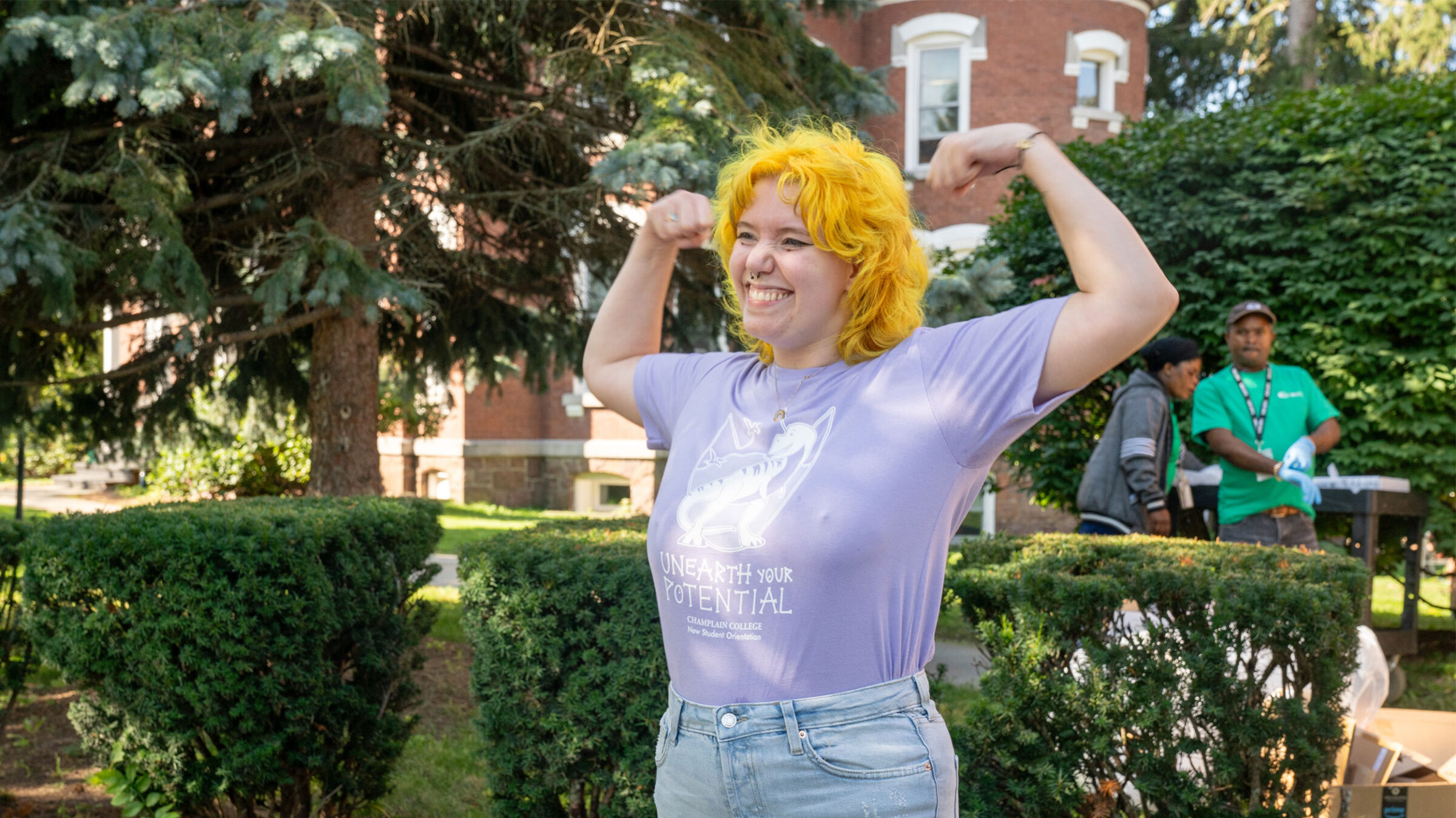 student in purple shirt and yellow hair holds their arms up in an "i'm strong" position