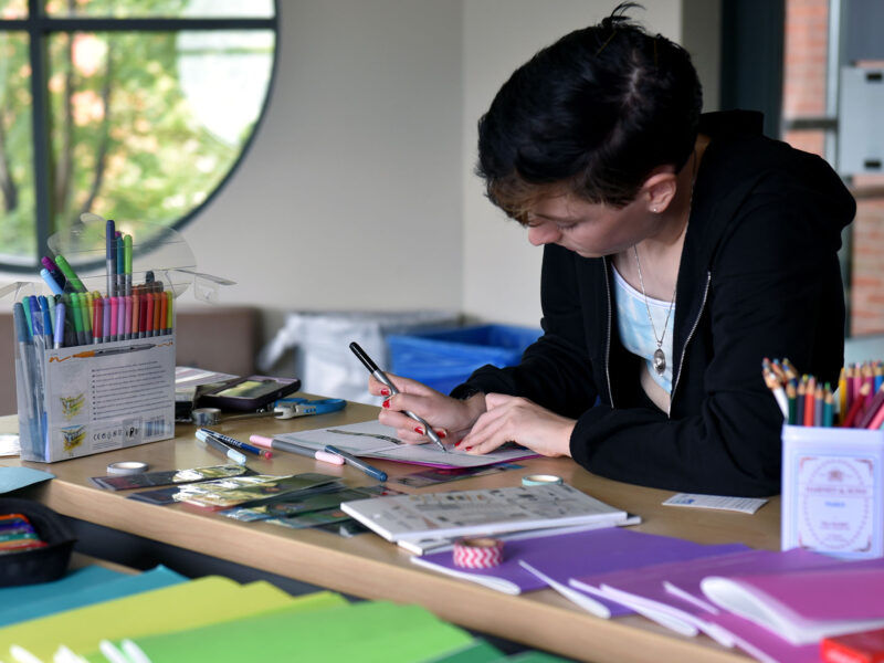 a student concentrates on writing in their gratitude journal. the table they're working on is covered in bright colored gratitude journals.