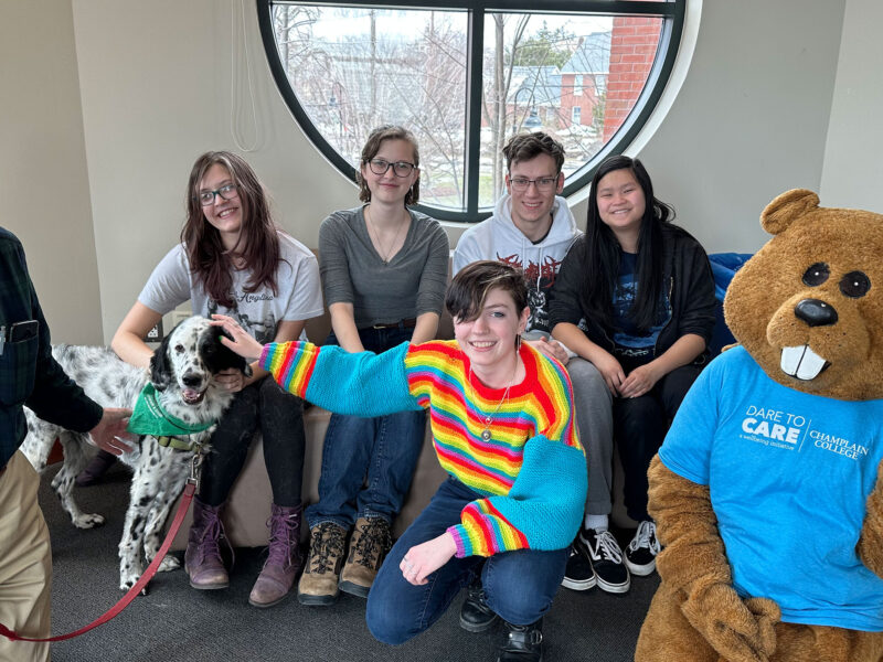 five students pose with Chauncey, a therapy dog, and the therapy dog's owner. the dog is white and black spotted.