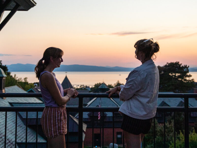 Two students in the Miller Information Commons Library at Champlain College overlooking Lake Champlain at sunset.