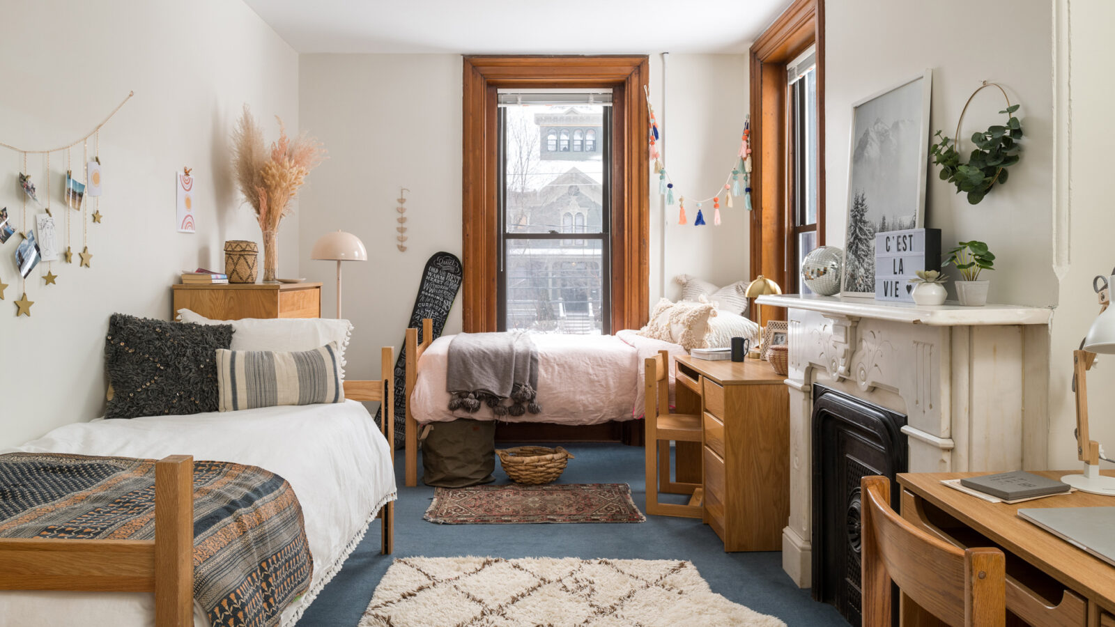 a dorm interior with two beds, two desks, and a fireplace