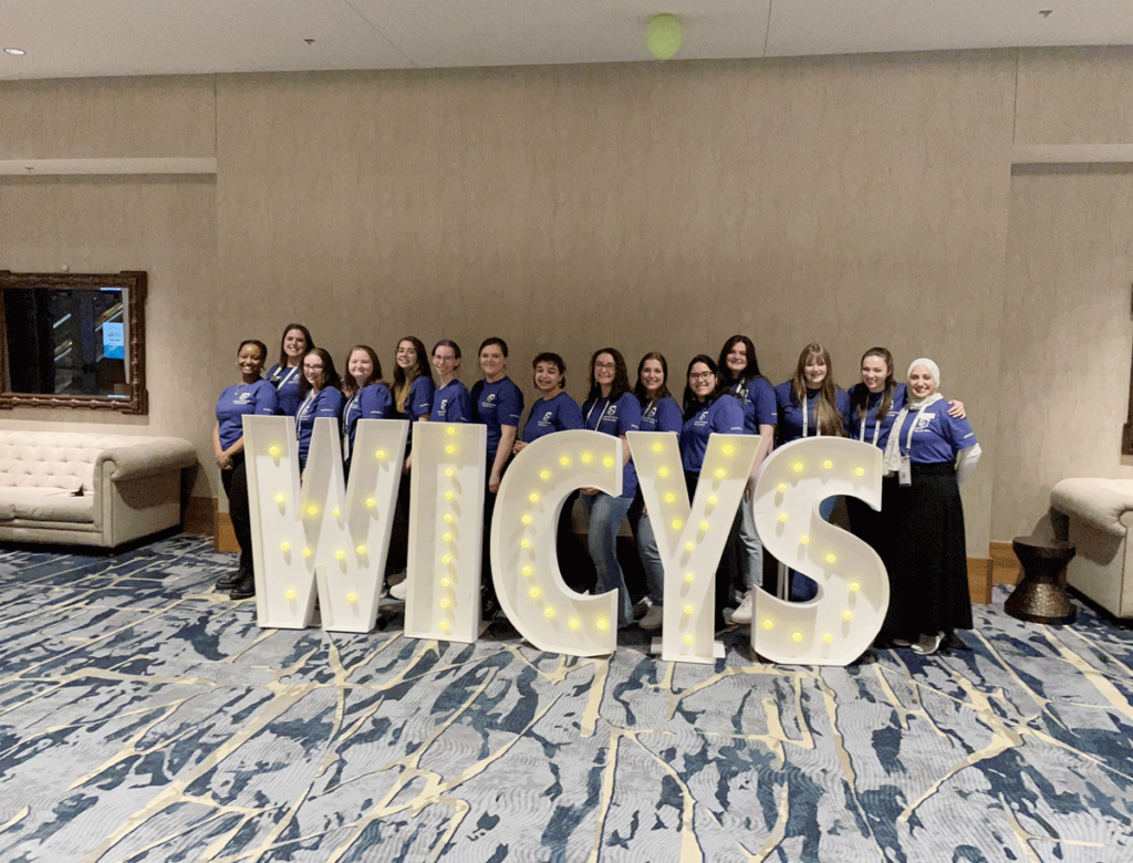 Female-identifying students from Champlain College pose with a light-up sign that reads "WICSY."