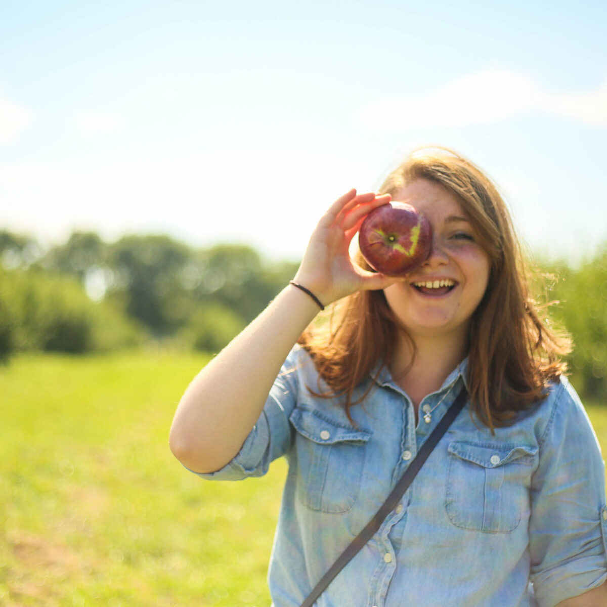 student holding an apple against their eye in a field