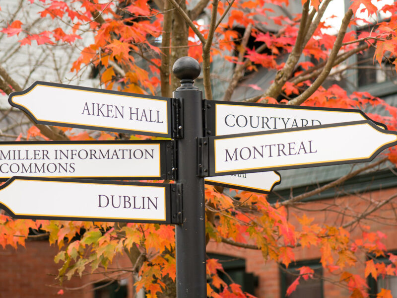 directional signs pointing in various directions including Montreal, Dublin, Miller Information Commons, Courtyard and Aiken Hall agains a backdrop of red-colored fall leaves