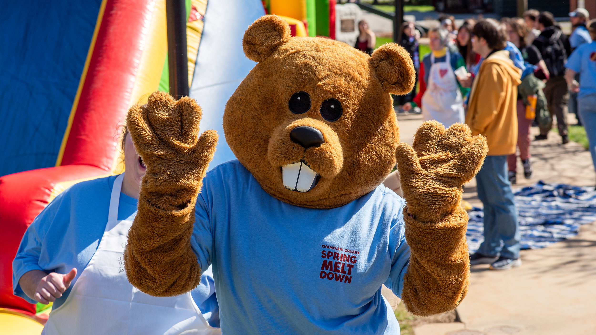 chauncey the beaver mascot holds both hands up in excitement with a big inflatable obstacle course behind him