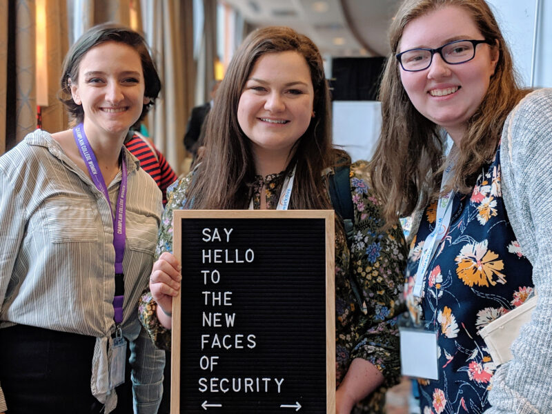 three female presenting students holding a sign that says "say hello to the new faces of security"