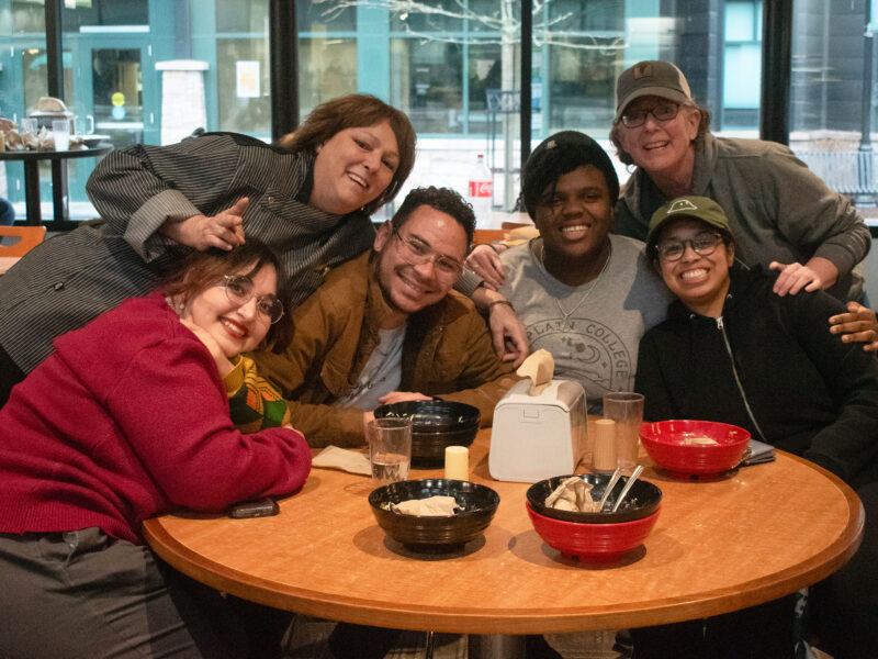 three students and two staff members smile big surrounding a table in the dining hall with a visiting chef