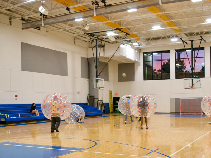 students play soccer in the gym while wearing big bubble inflatable outerwear