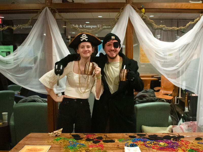 two students wear pirate hats and costumes at a table filled with mardi gras beads