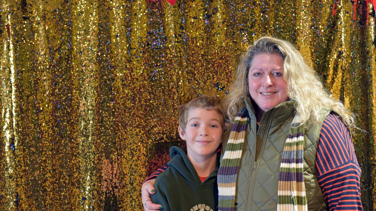 a mom and her son pose in front of a gold glitter backdrop
