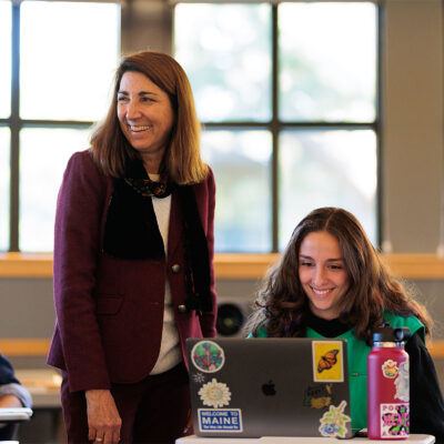 Female student smiling at her laptop next to her smiling professor