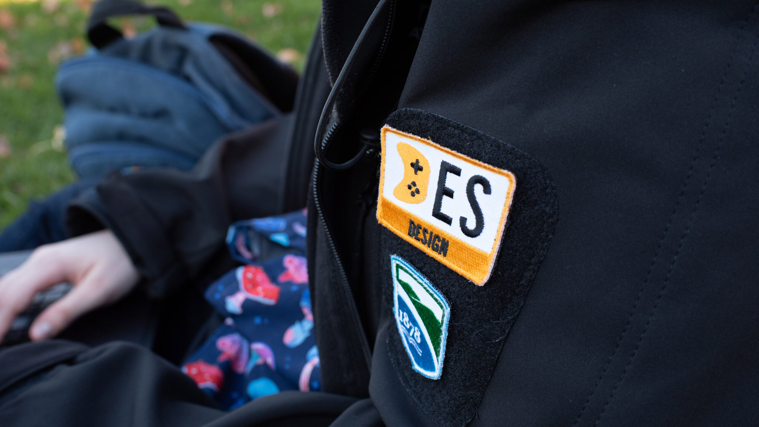 Close up photo of a student wearing a Game design jacket outside with patches