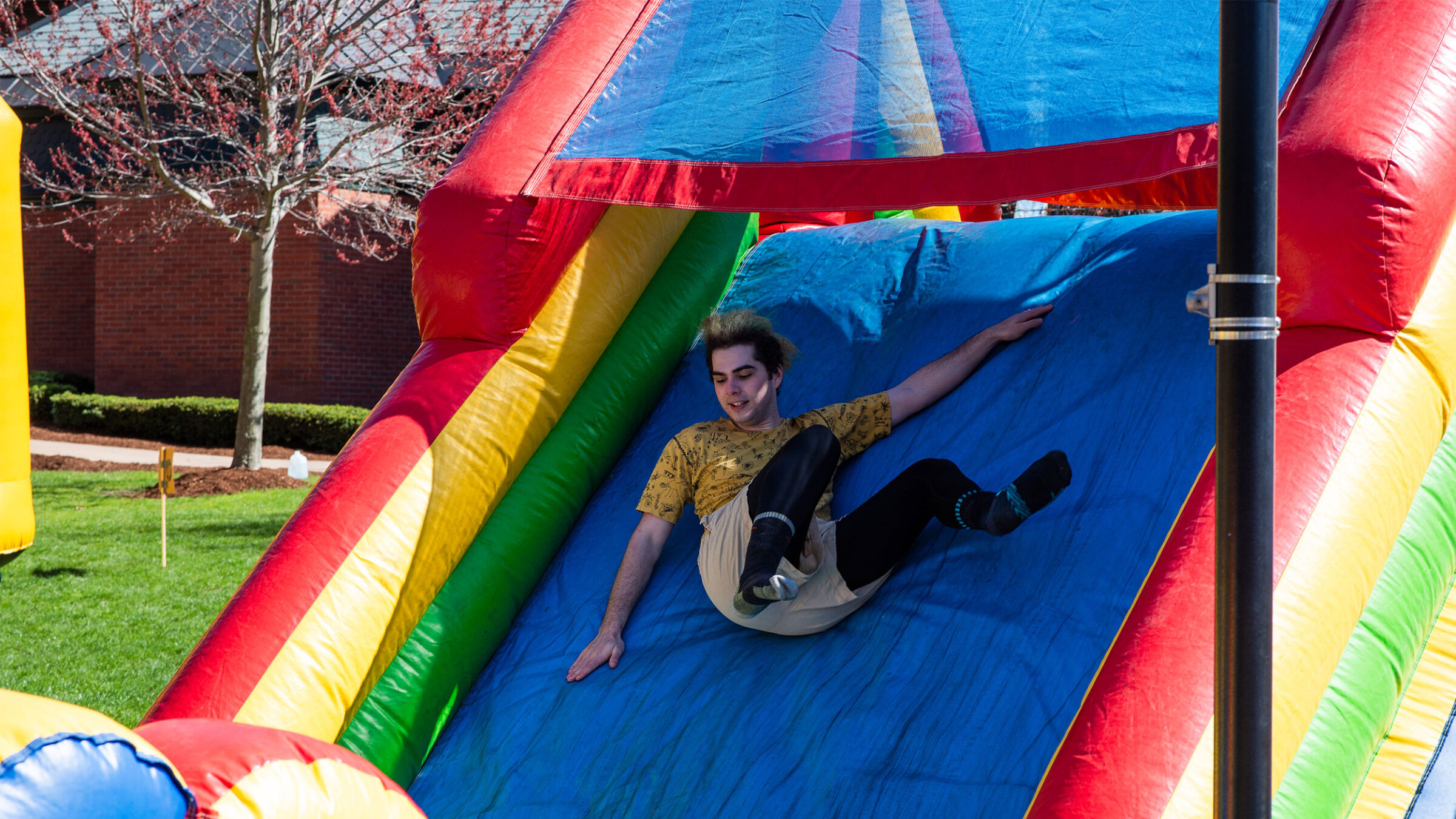 a student slides down an inflatable bouncy house slide that is blue, red, green, and yellow