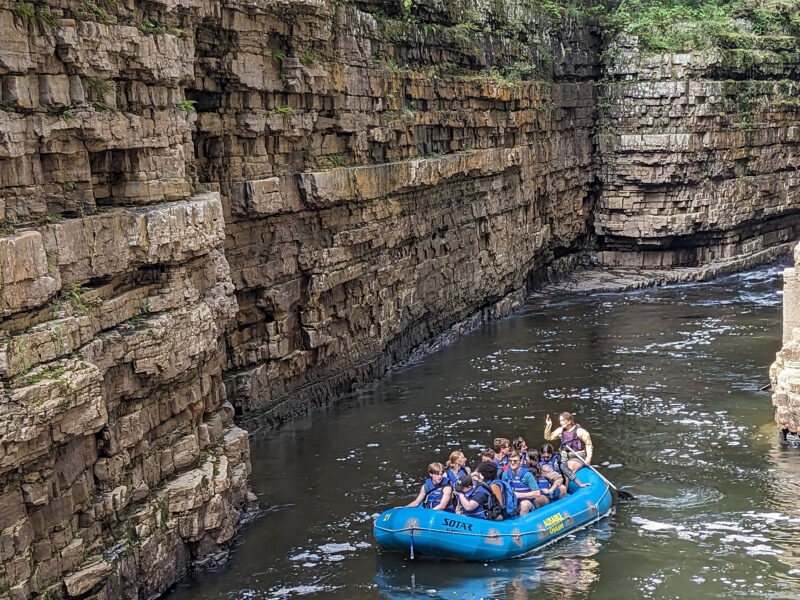 a group of students raft down the river surrounded by high walls of rock
