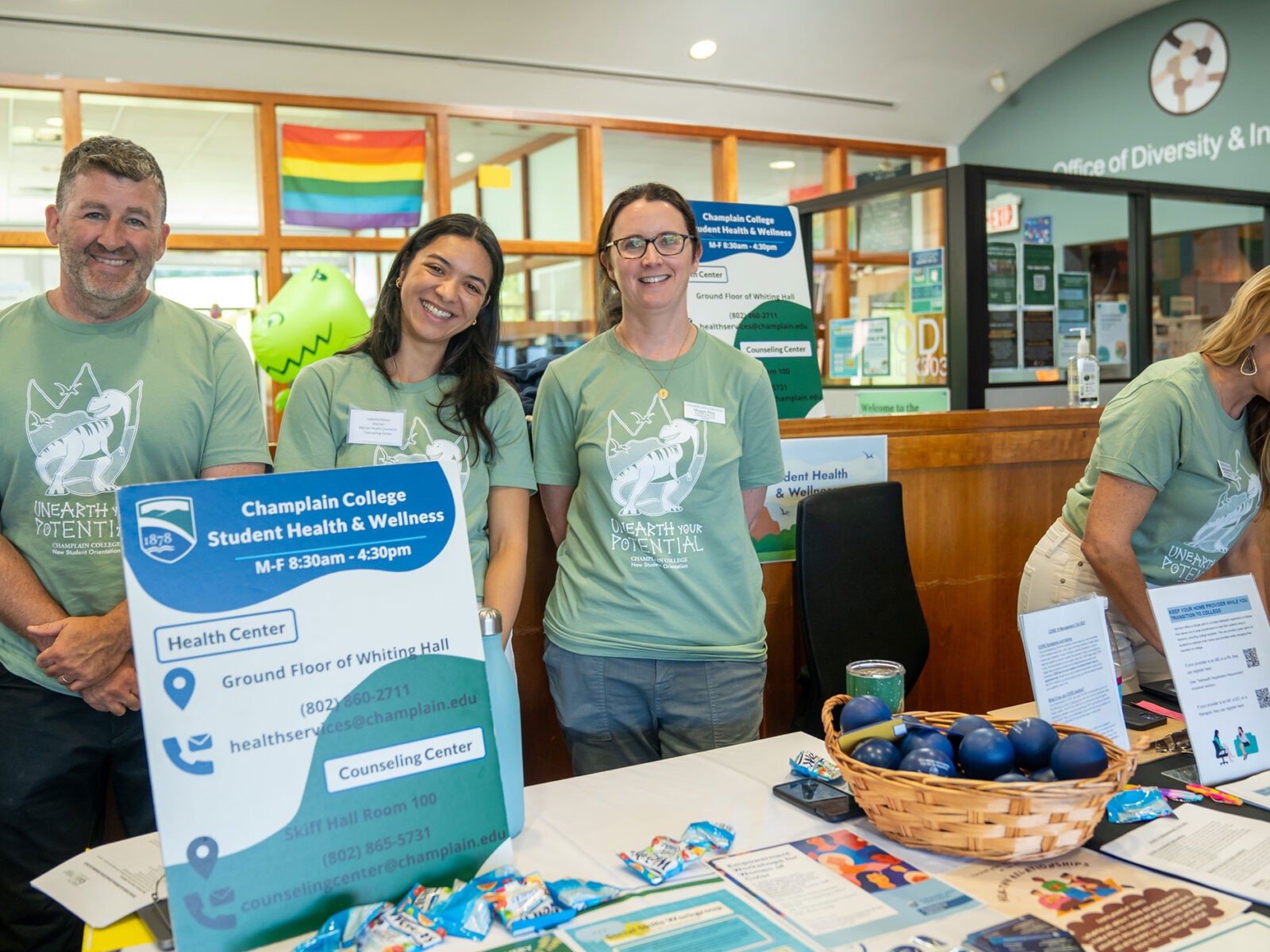 three members of the counseling center team smile in green t-shirts behind a table decked out in informational posters and pamphlets about the services they offer