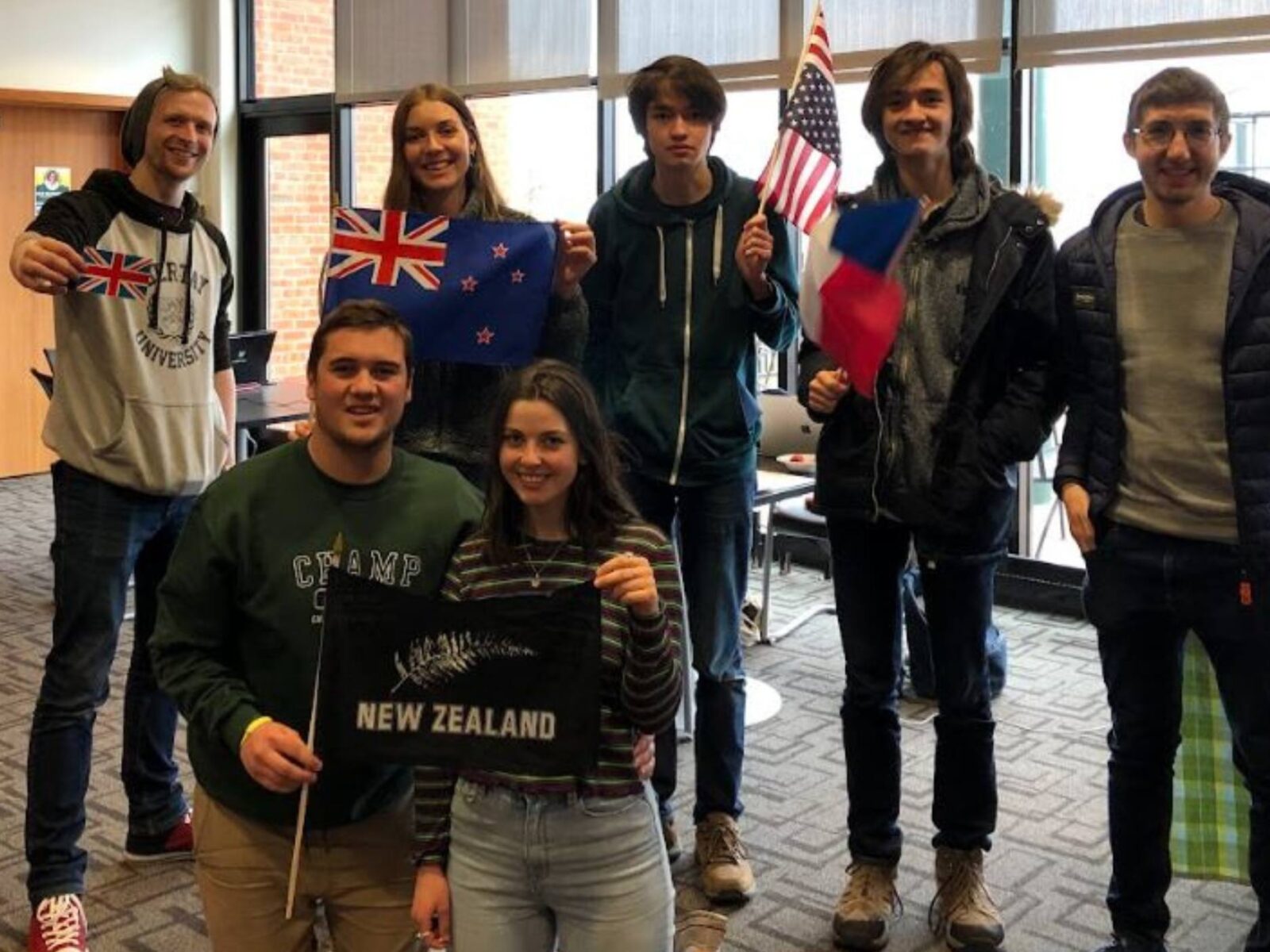 Students in the exchange program in fireside lounge holding flags from study abroad countries