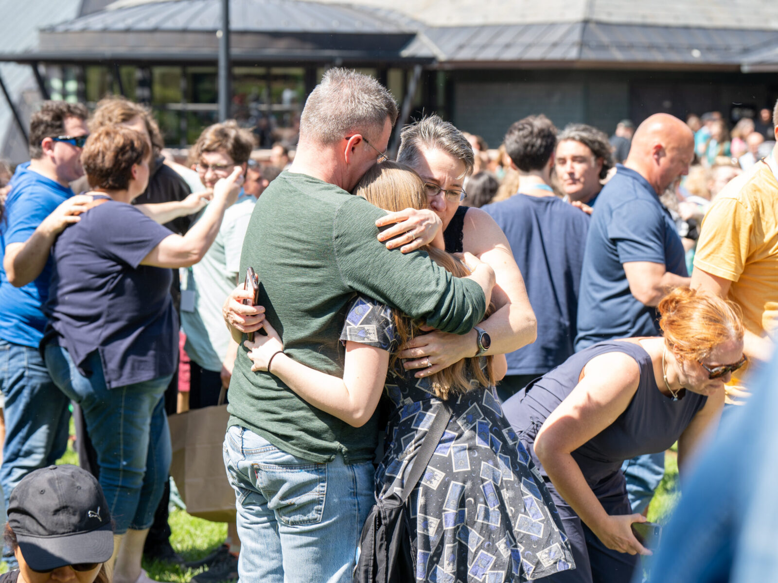 a student hugs two adults as they say goodbye to each other on a crowded aiken lawn