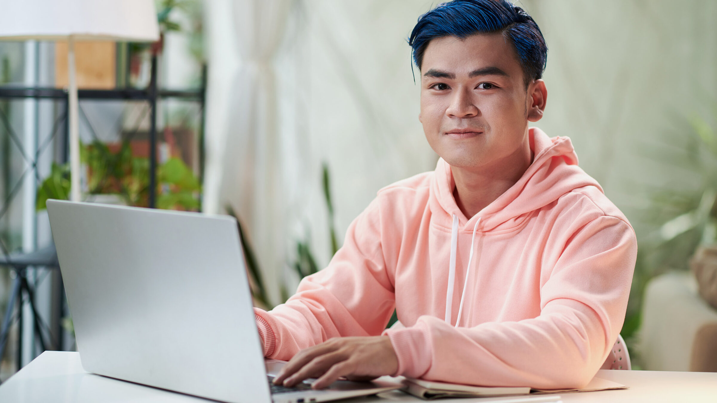 young man with blue hair is using a laptop
