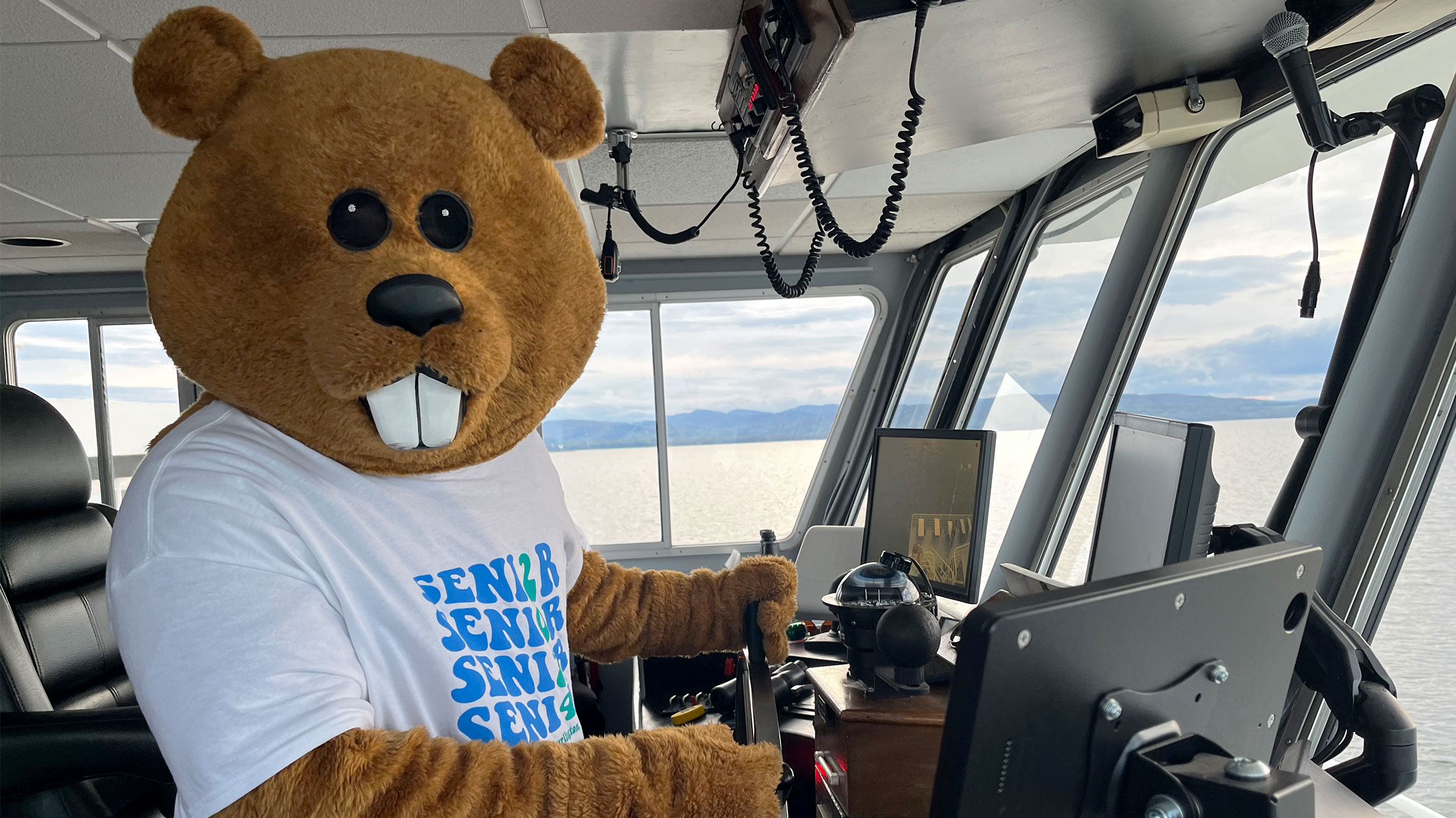 mascot chauncey t. beaver captains the ethan allen boat cruise with a lake and mountain view through the boat window