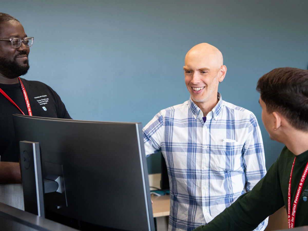 three people smiling in the leahy center while looking at a computer screen