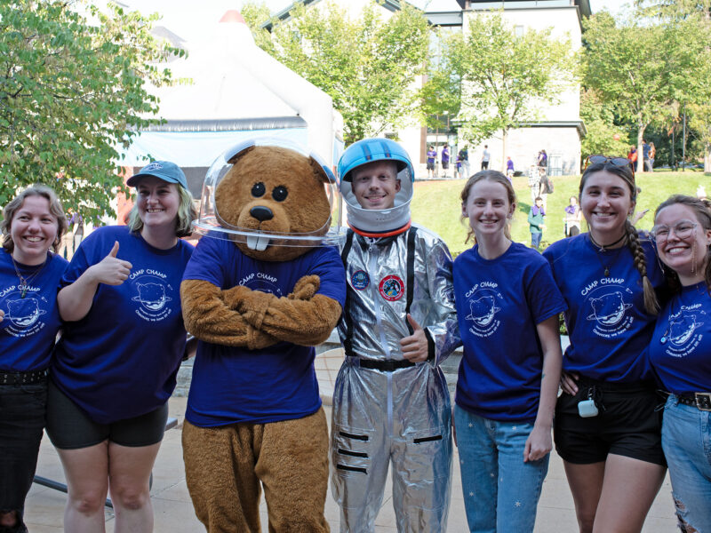 Five students who are part of CHAMP pose for a photo in purple t-shirts with Chauncey T Beaver. One student is in a silver astronaut costume.