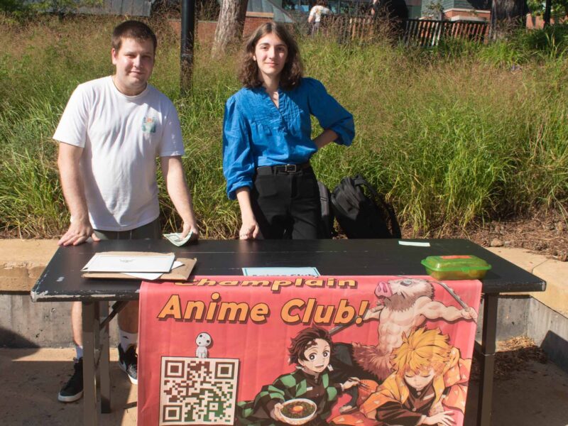 students stand behind a table promoting the anime club at champlain during the activity fair