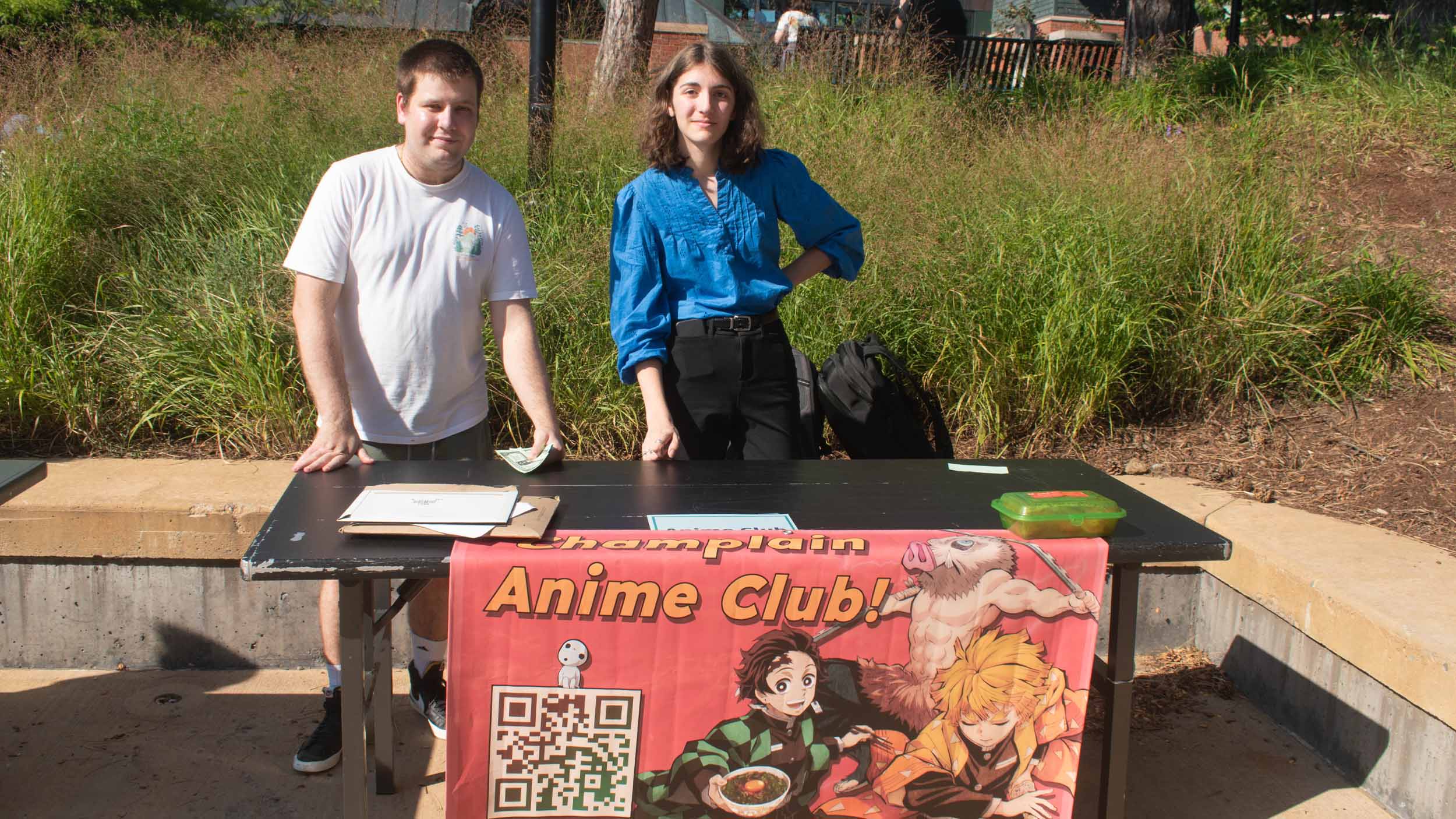 students stand behind a table promoting the anime club at champlain during the activity fair