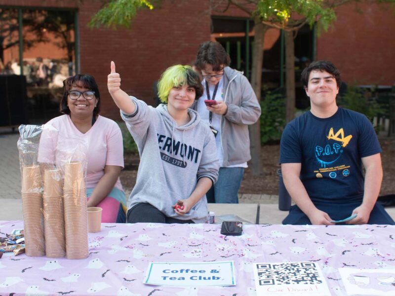 students giving a thumbs up and smiling while sitting at the coffee and tea club table at Champlain's Activity Fair