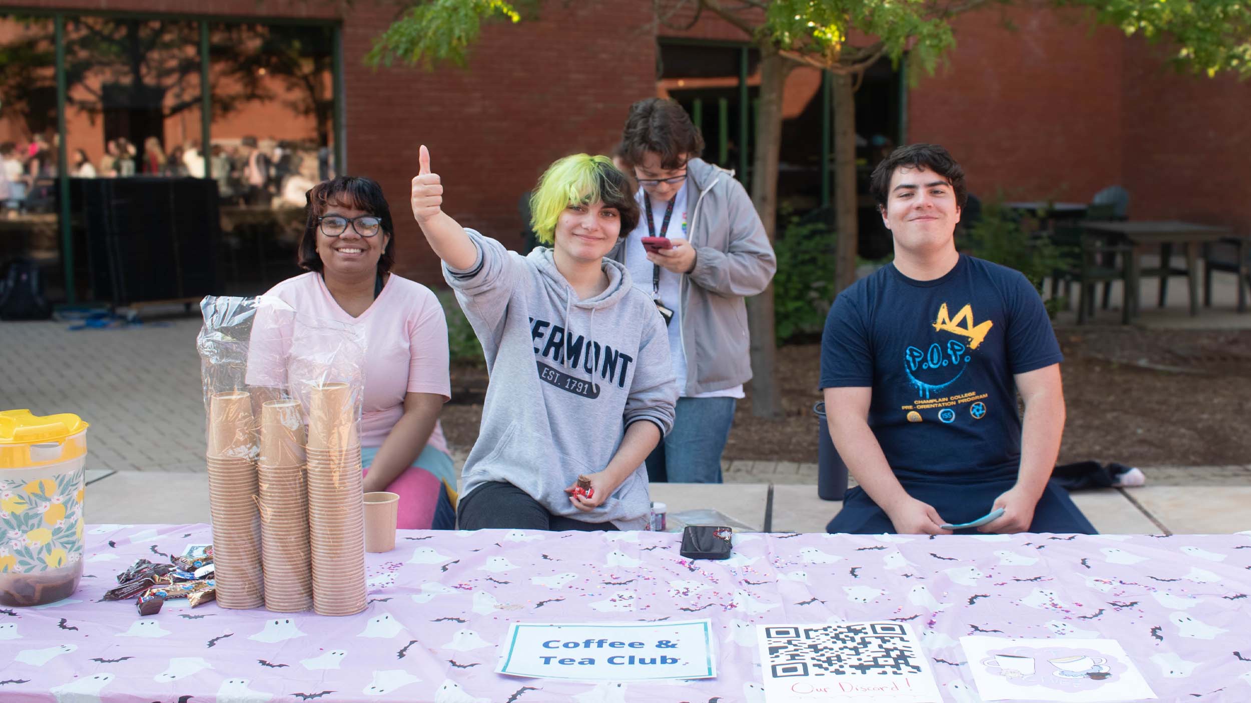 students giving a thumbs up and smiling while sitting at the coffee and tea club table at Champlain's Activity Fair