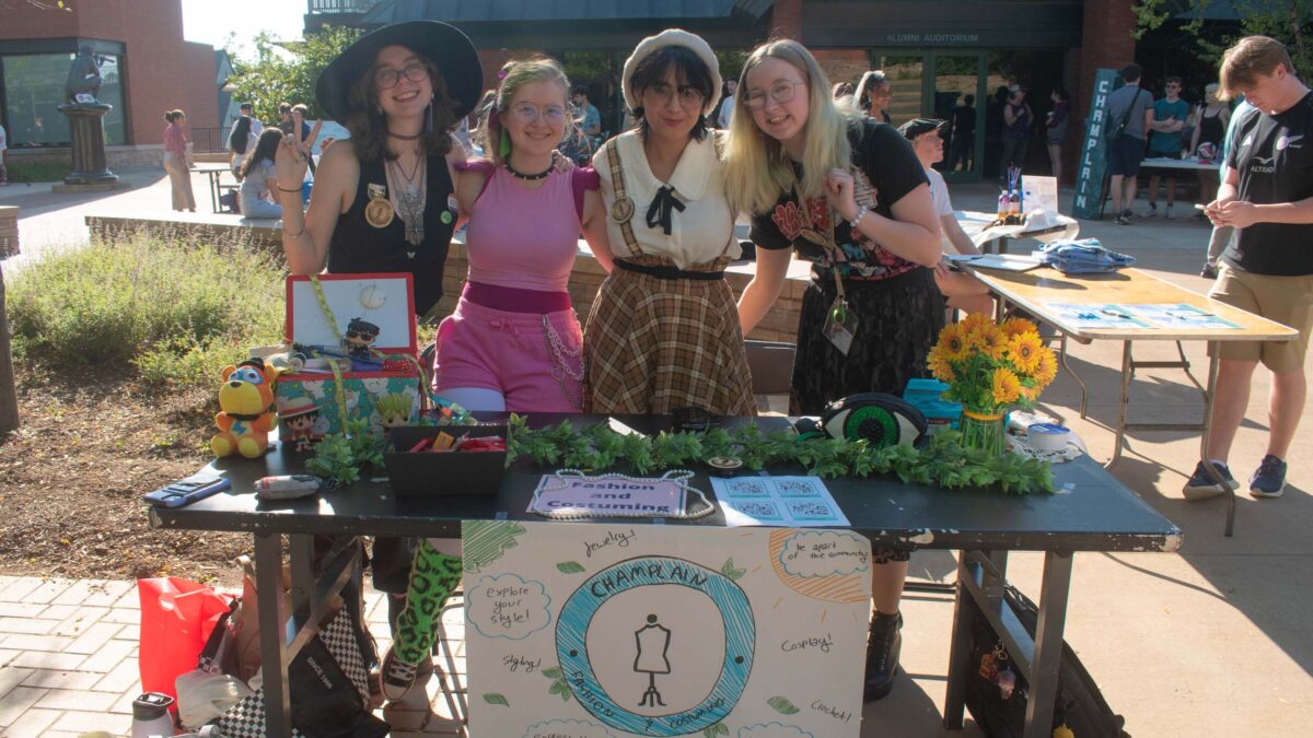 students in the Champlain Fashion and Costuming club posing behind their decorated table at the activities fair