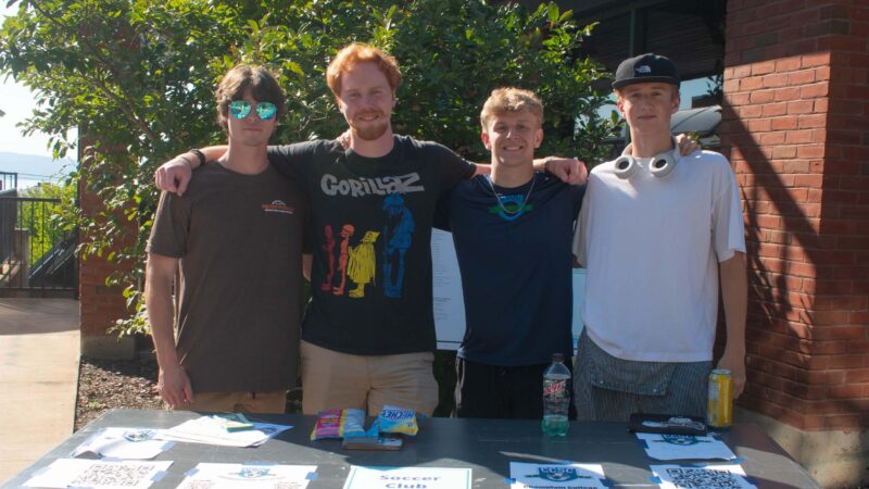 students in the Champlain Soccer Club standing behind a table at the activity fair posing for a photo