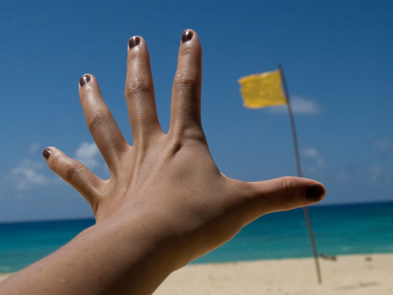 a hand reaching toward a flag on the beach