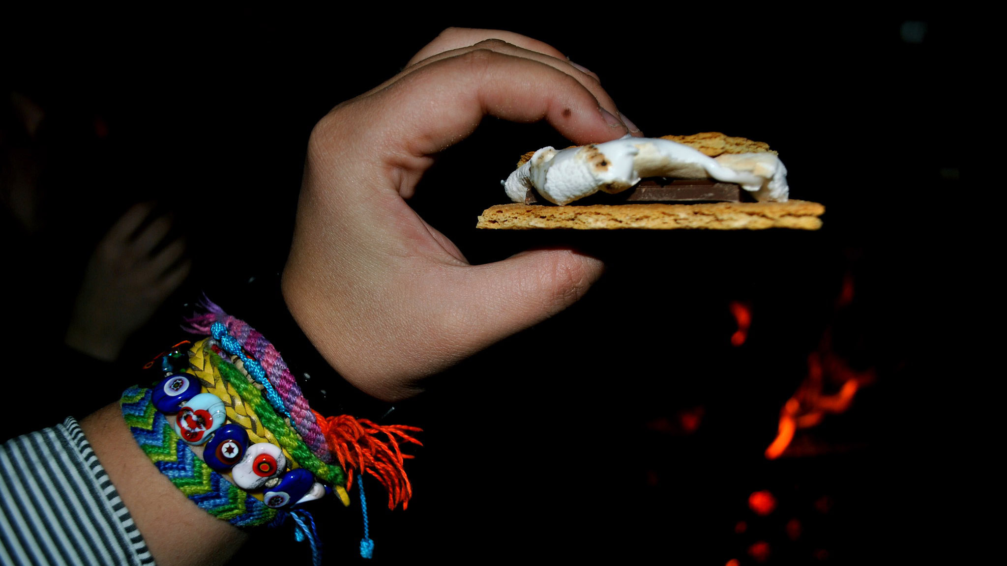 a person holding a smore wearing bracelets in the dark