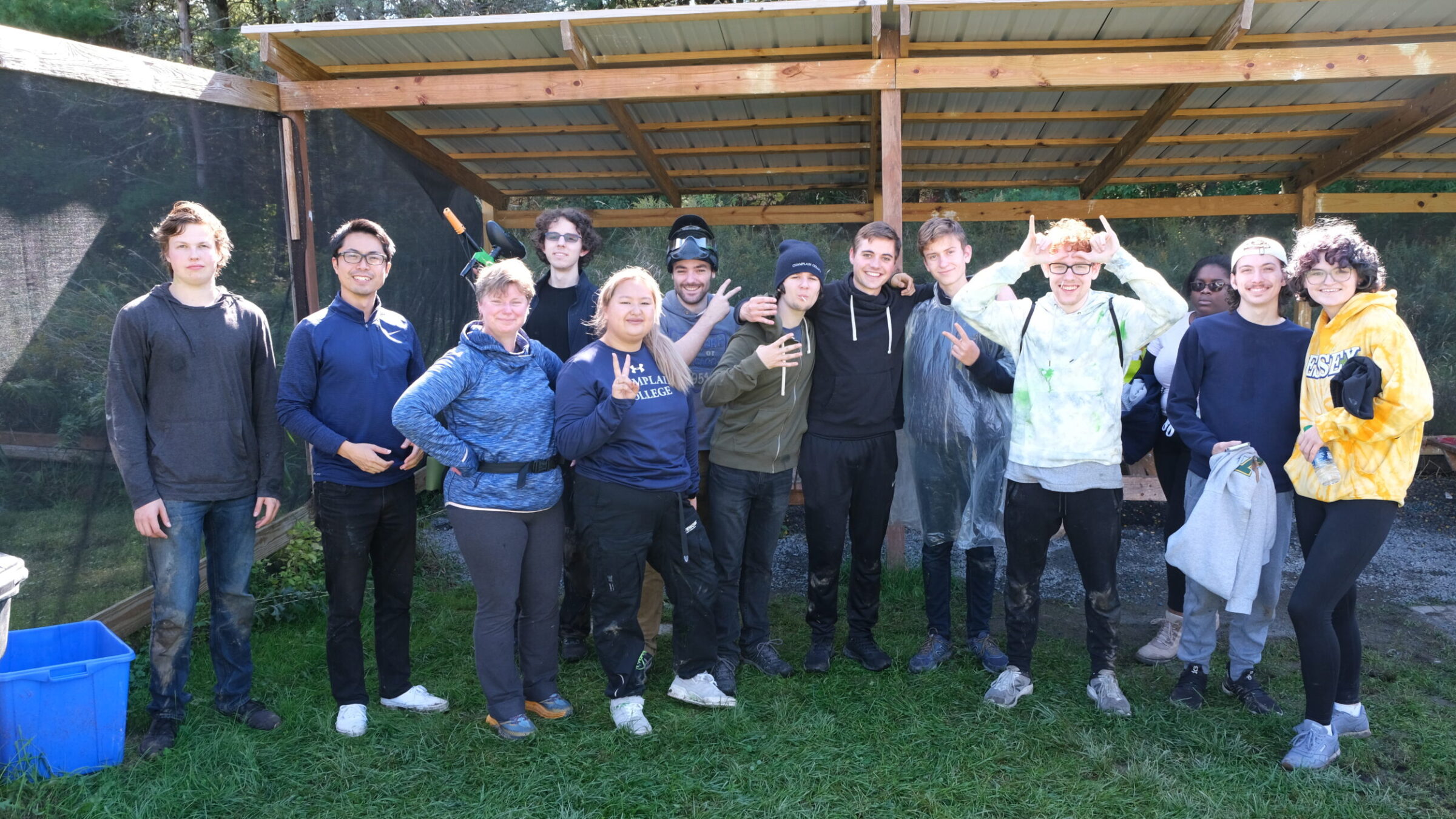 A group of students and staff at a paintball field smiling for a photo