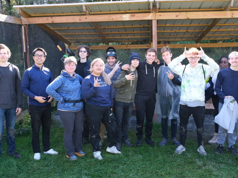 A group of students and staff at a paintball field smiling for a photo