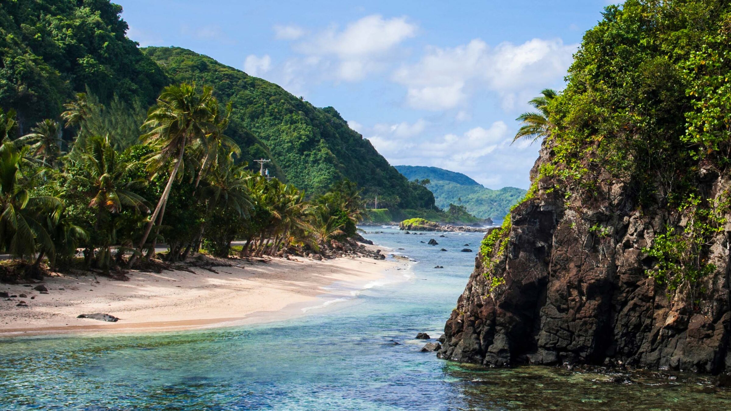 sandy beach and ocean surrounded by green cliffs and mountains