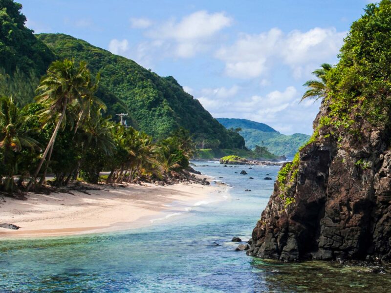 sandy beach and ocean surrounded by green cliffs and mountains