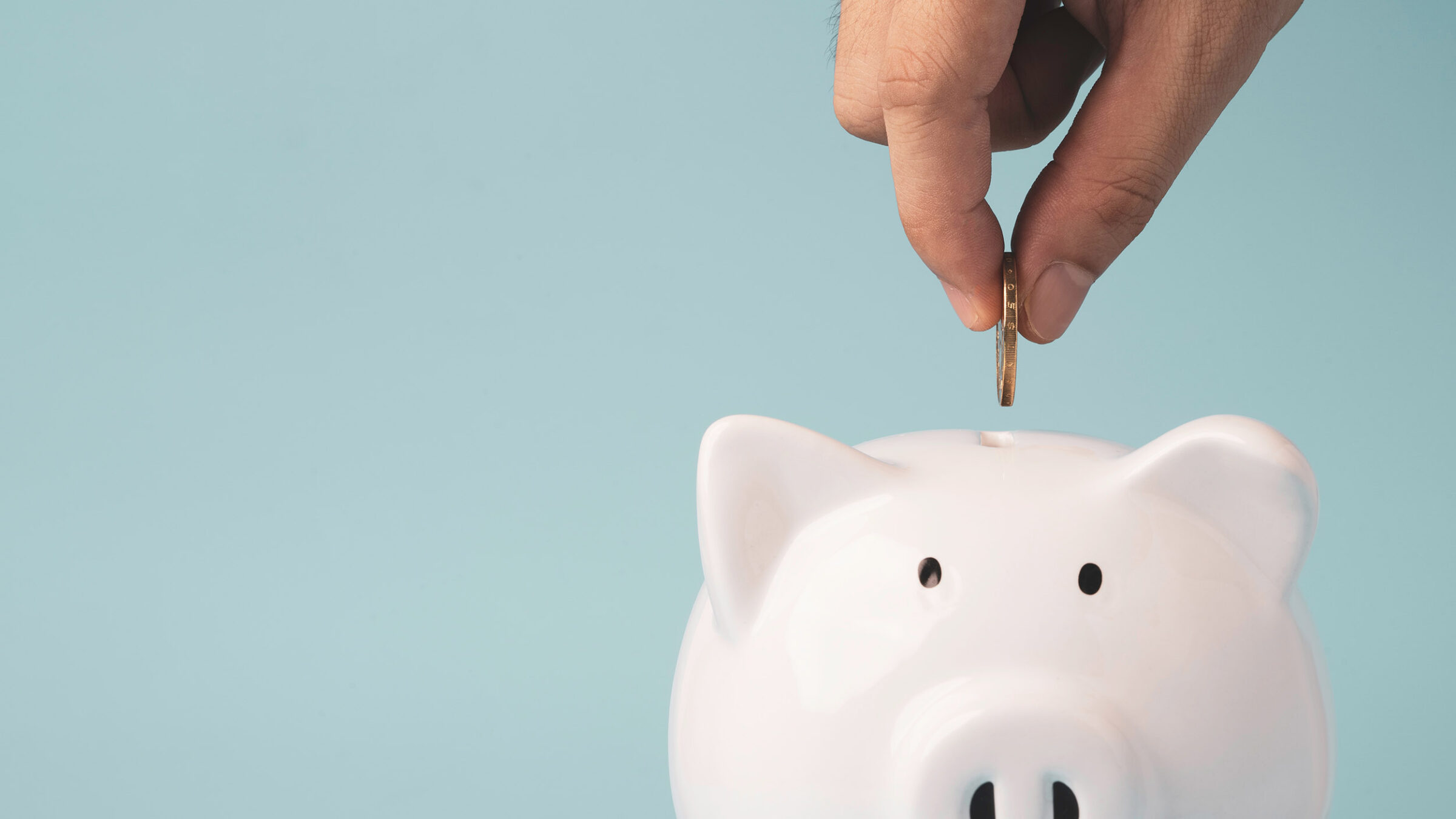 Hand putting coin to white piggy bank saving on blue background