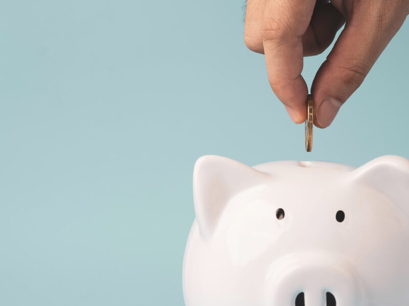 Hand putting coin to white piggy bank saving on blue background