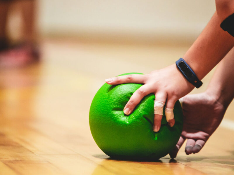 a person grabbing a green dodgeball in a gym