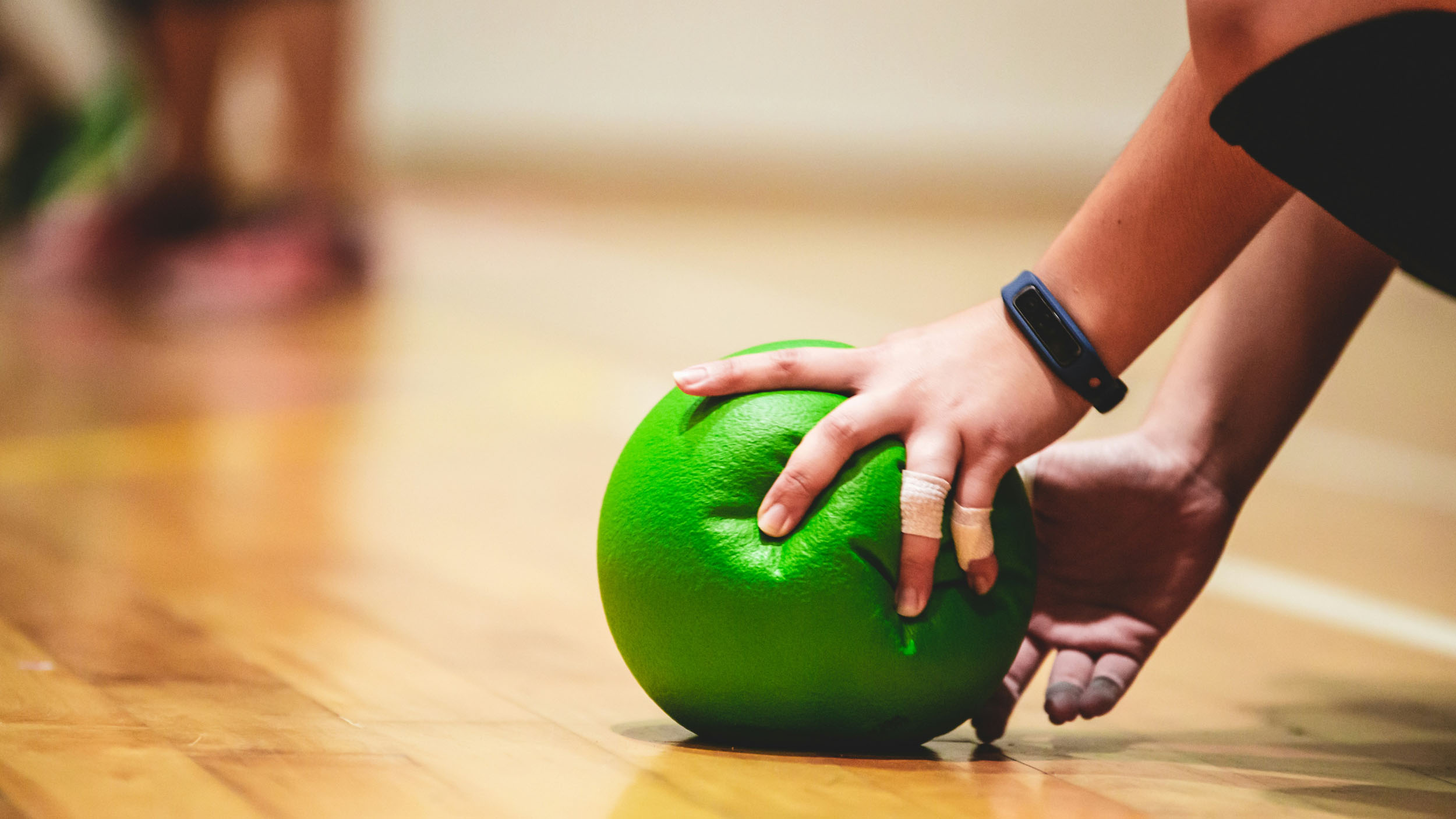 a person grabbing a green dodgeball in a gym