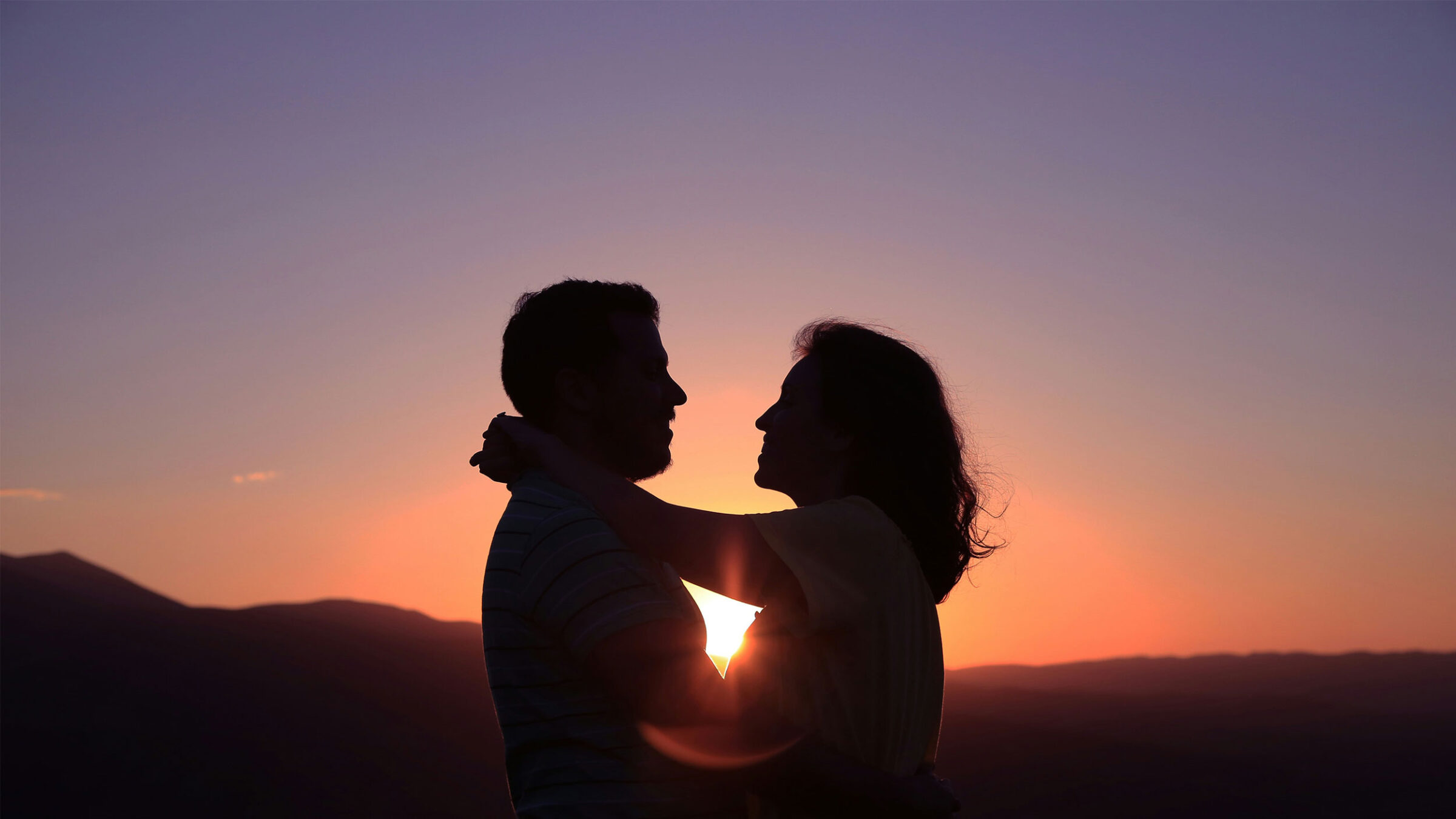 a couple holds on to each other in front of the sunset