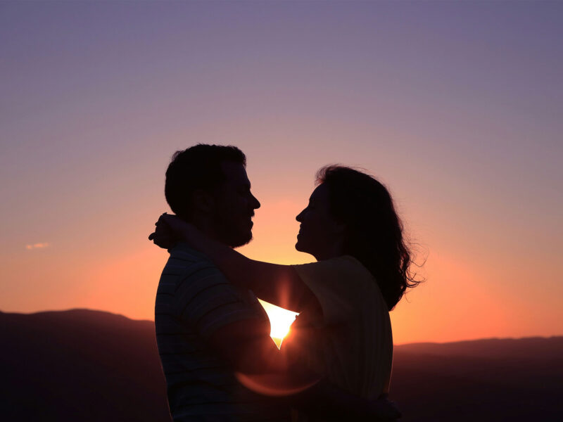 a couple holds on to each other in front of the sunset