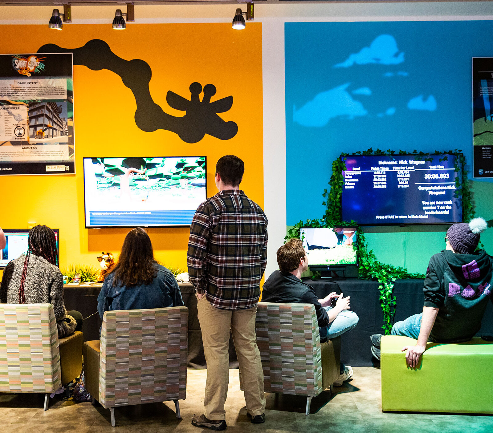 students sit in chairs playing games in front of a colorful gallery wall