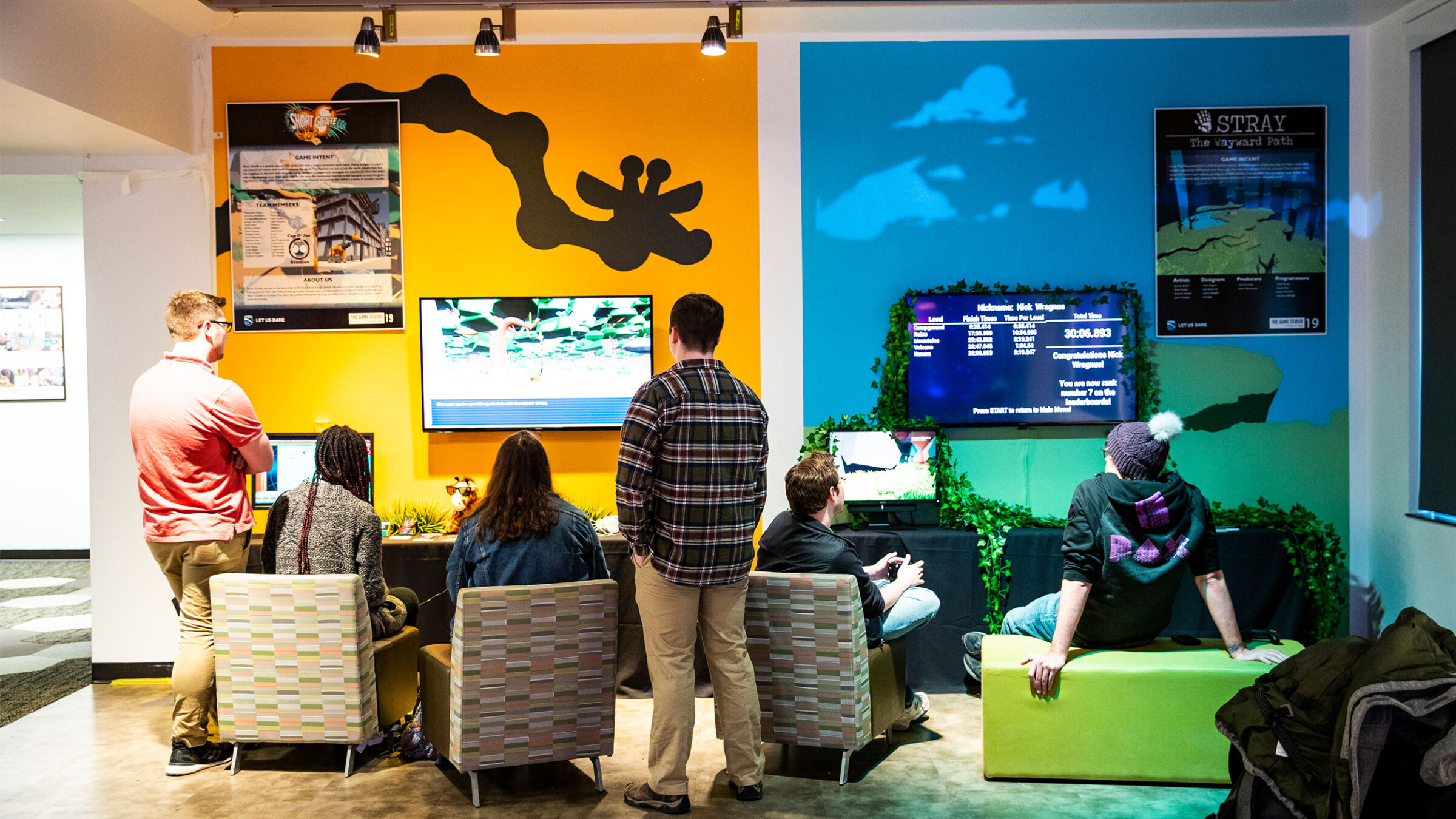 students sit in chairs playing games in front of a colorful gallery wall