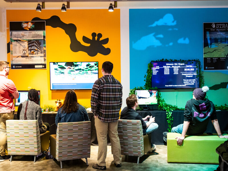 students sit in chairs playing games in front of a colorful gallery wall