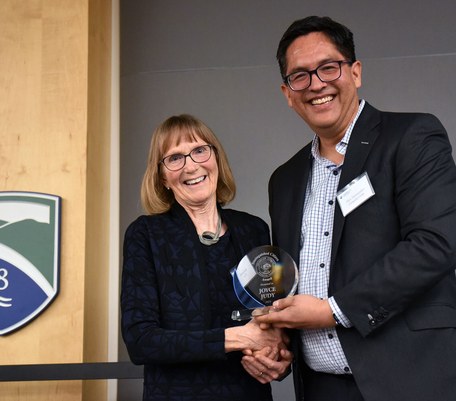 joyce judy and alex hernandez shake hands on stage while holding joyce's award