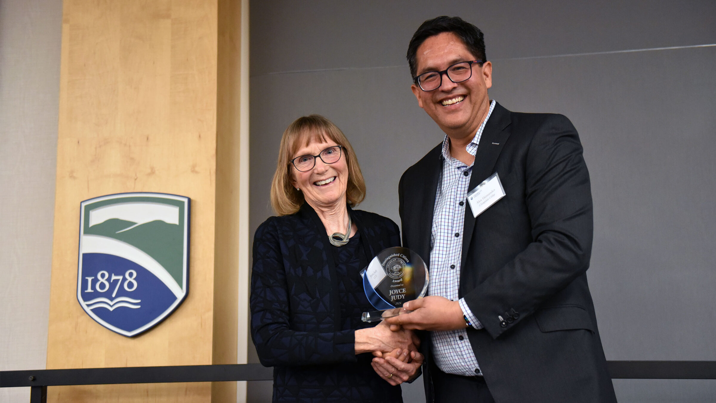 joyce judy and alex hernandez shake hands on stage while holding joyce's award